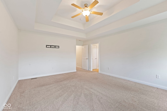 empty room featuring a raised ceiling, ceiling fan, and light colored carpet