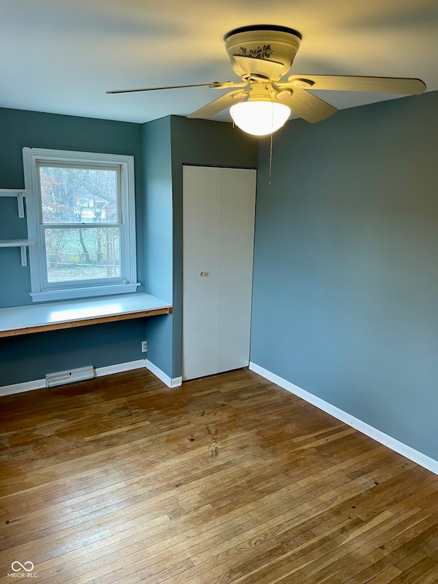 unfurnished bedroom featuring ceiling fan, a closet, built in desk, and hardwood / wood-style flooring