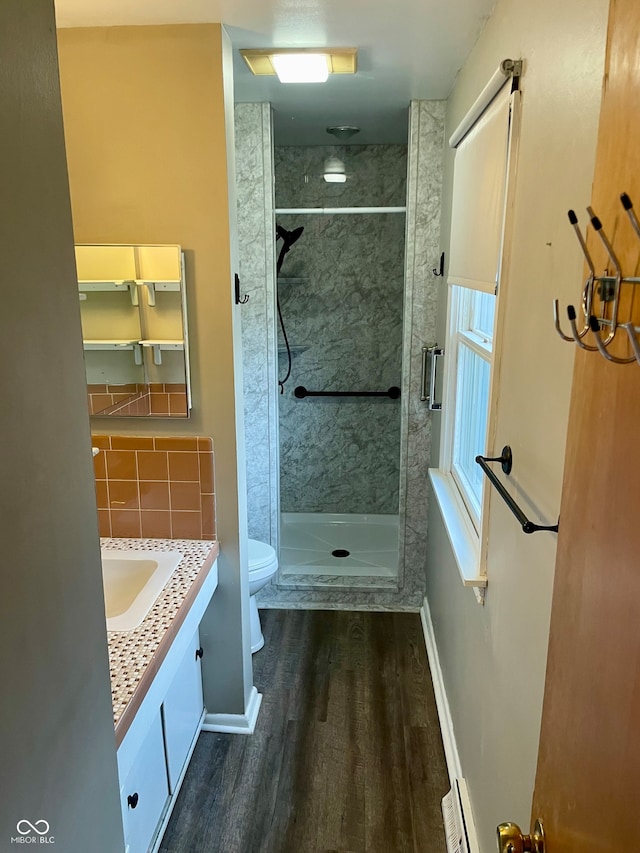 bathroom featuring tasteful backsplash, vanity, tiled shower, wood-type flooring, and toilet