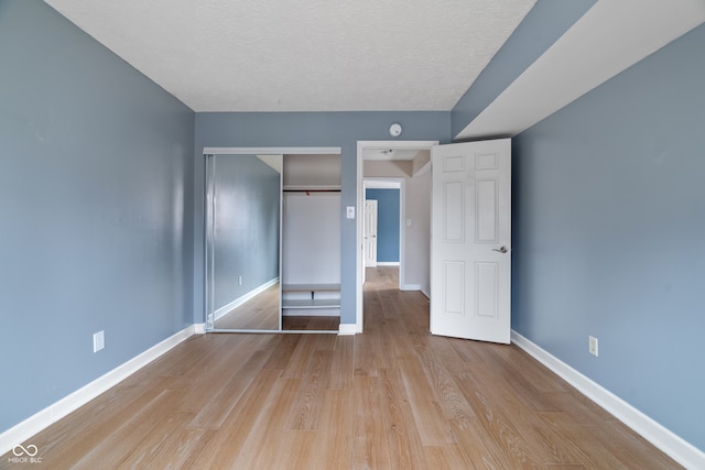 unfurnished bedroom with light wood-type flooring, a textured ceiling, and a closet