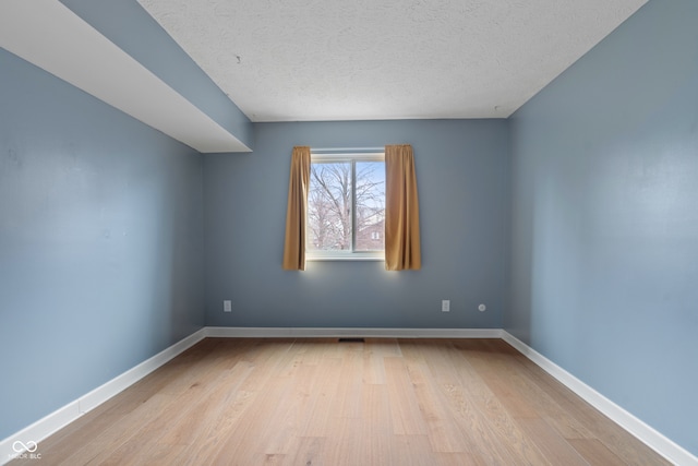 empty room with a textured ceiling and light hardwood / wood-style flooring