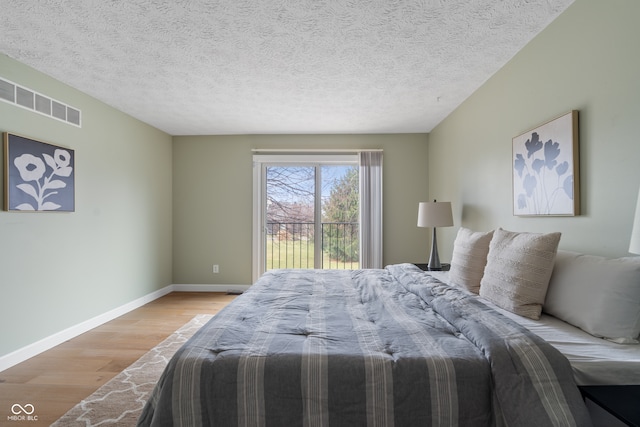 bedroom with light wood-type flooring, a textured ceiling, and access to outside