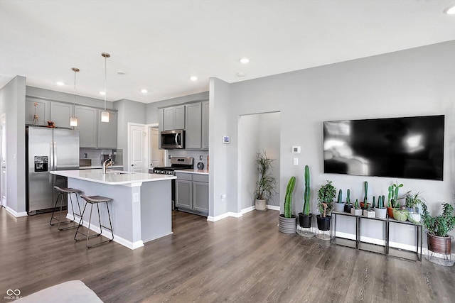 kitchen featuring decorative light fixtures, stainless steel appliances, gray cabinets, and a kitchen island with sink