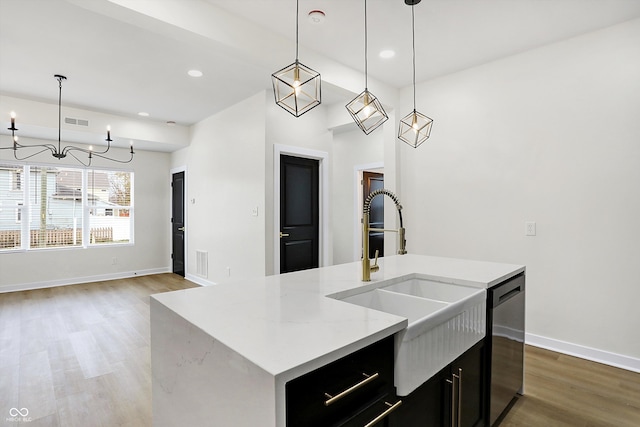 kitchen featuring dishwasher, sink, hanging light fixtures, hardwood / wood-style floors, and a center island with sink