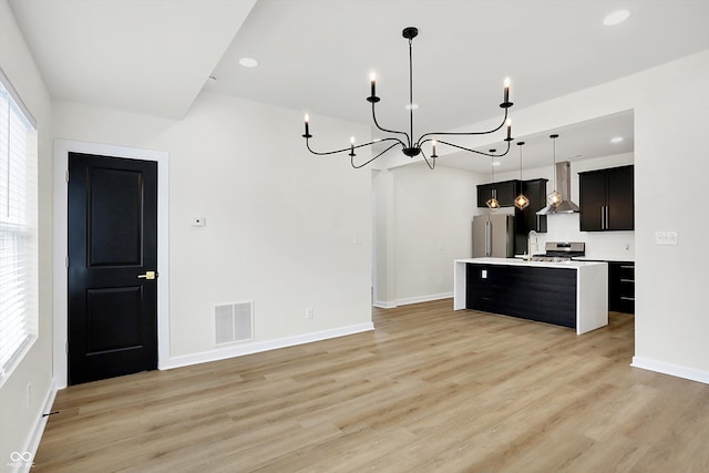 kitchen featuring light hardwood / wood-style floors, a center island with sink, hanging light fixtures, and appliances with stainless steel finishes