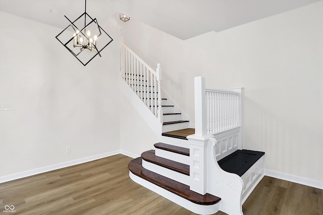 stairway with wood-type flooring and an inviting chandelier