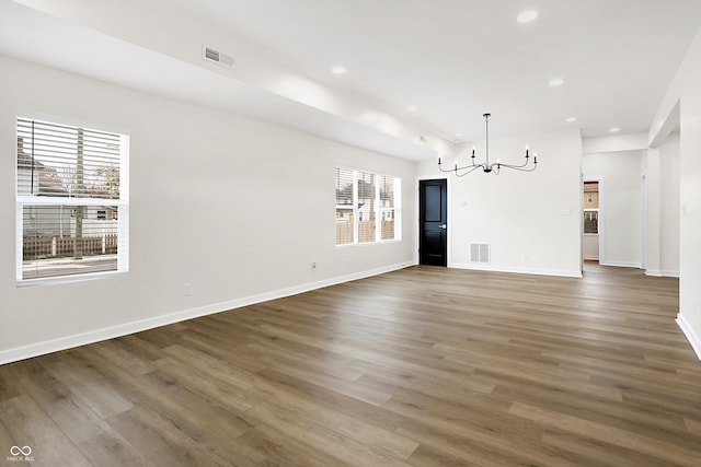 spare room featuring plenty of natural light, dark hardwood / wood-style floors, and an inviting chandelier