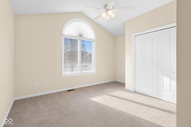 unfurnished bedroom featuring ceiling fan, a closet, light colored carpet, and lofted ceiling