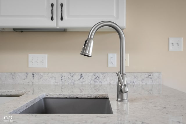 details featuring light stone counters, white cabinetry, and sink