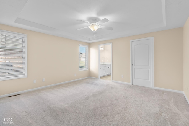 unfurnished bedroom with ensuite bathroom, ceiling fan, light colored carpet, and multiple windows