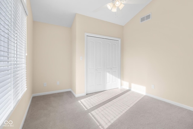 unfurnished bedroom with light colored carpet, a closet, lofted ceiling, and ceiling fan