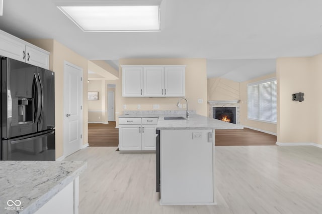 kitchen with white cabinetry, sink, light stone countertops, light hardwood / wood-style flooring, and stainless steel refrigerator with ice dispenser