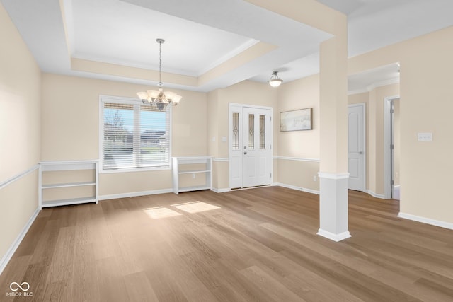 interior space featuring a raised ceiling, ornamental molding, a notable chandelier, and hardwood / wood-style flooring