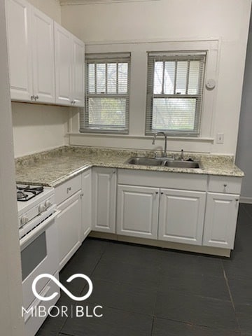 kitchen featuring white range with gas stovetop, white cabinets, dark tile patterned floors, and sink