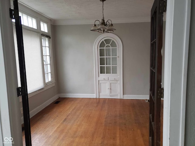 unfurnished dining area featuring hardwood / wood-style flooring, a notable chandelier, crown molding, and a textured ceiling