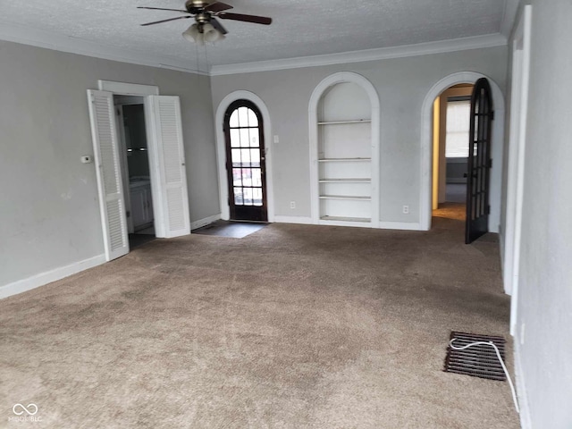 empty room featuring crown molding, built in features, carpet floors, and a wealth of natural light