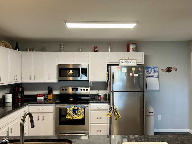 kitchen with white cabinets, stainless steel appliances, dark stone countertops, and sink