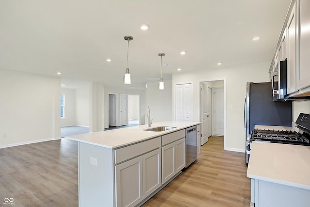 kitchen featuring decorative light fixtures, a center island with sink, sink, light hardwood / wood-style flooring, and appliances with stainless steel finishes