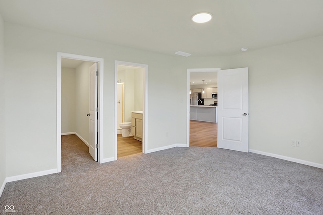 unfurnished bedroom featuring light carpet, stainless steel fridge with ice dispenser, and connected bathroom