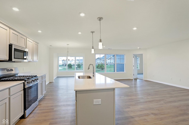 kitchen featuring a center island with sink, sink, hanging light fixtures, light wood-type flooring, and appliances with stainless steel finishes