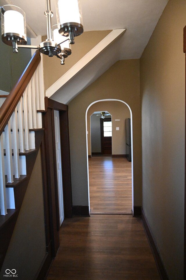 hall with dark wood-type flooring, vaulted ceiling, and a notable chandelier