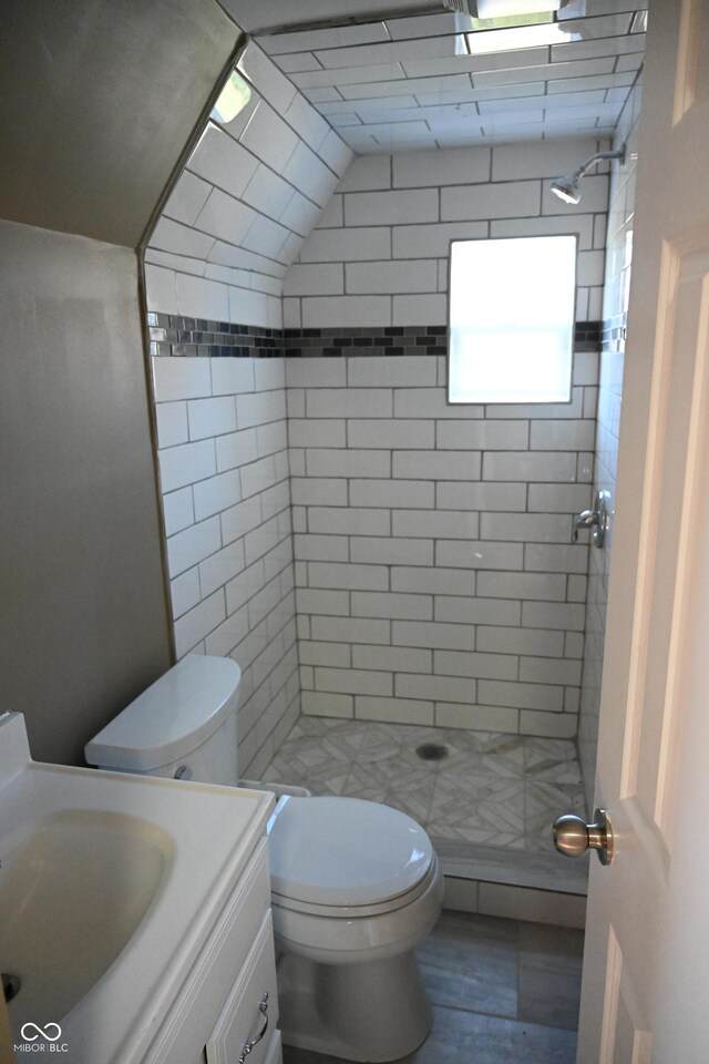 bathroom featuring a tile shower, vanity, lofted ceiling, and toilet