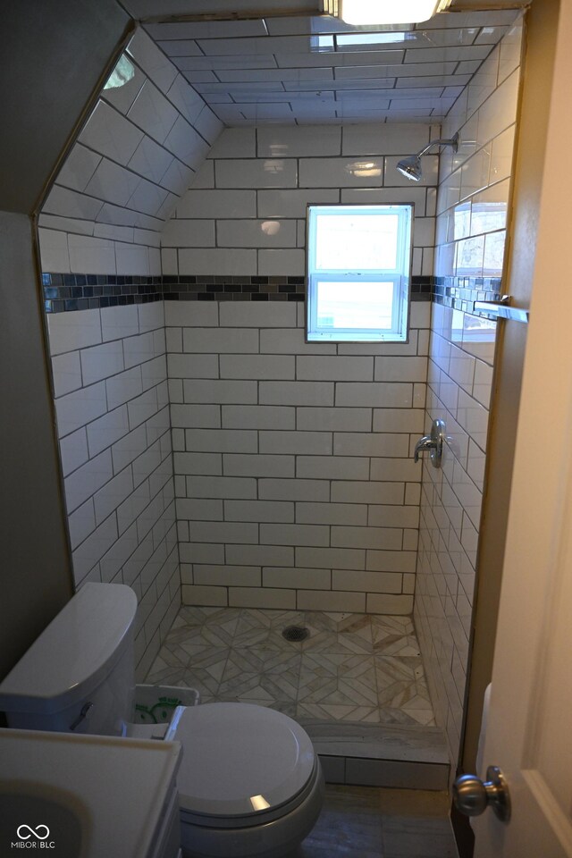 bathroom featuring a tile shower, vanity, vaulted ceiling, and toilet