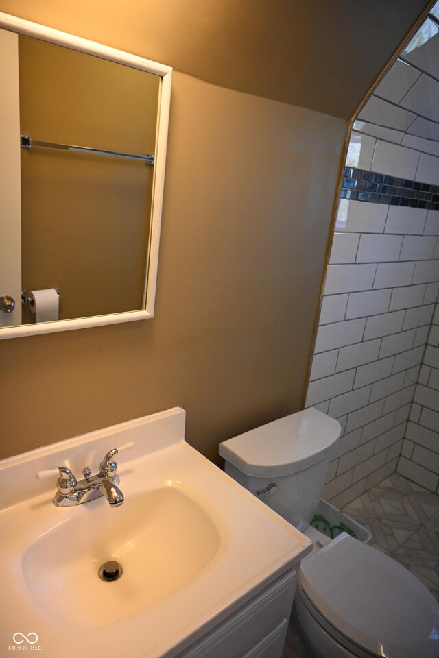 bathroom with tiled shower, vanity, and toilet