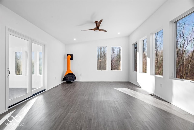 interior space featuring a wood stove, ceiling fan, dark hardwood / wood-style flooring, and vaulted ceiling