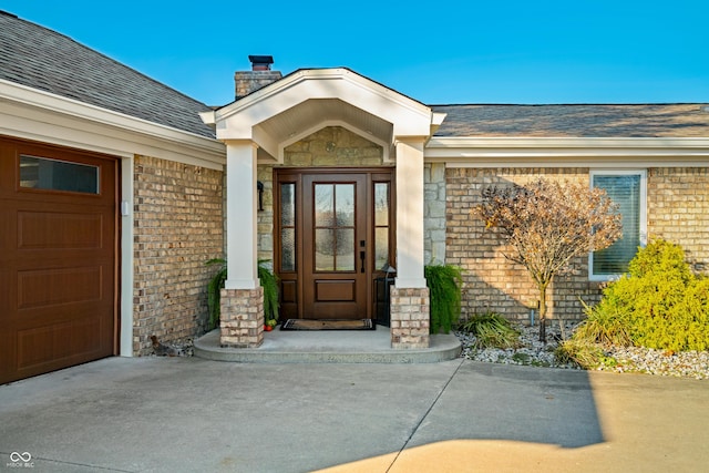 9454 Raintree Dr S, Columbus, IN 47201 - view of exterior entry featuring a chimney, brick siding, a shingled roof, and concrete driveway