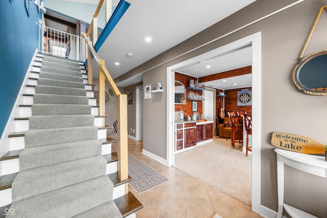 stairs with carpet, beam ceiling, and bar area