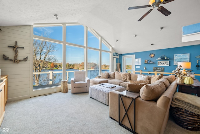 carpeted living room with lofted ceiling, a water view, wooden walls, ceiling fan, and a textured ceiling