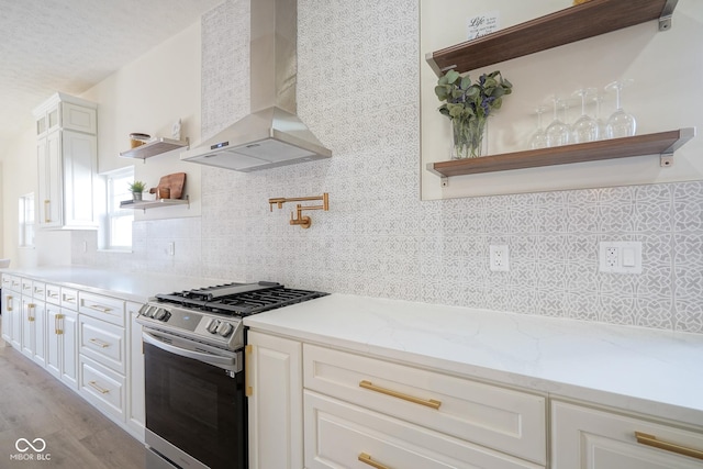 kitchen with stainless steel gas stove, white cabinetry, backsplash, light stone counters, and exhaust hood