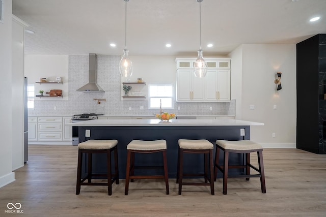 kitchen with gas range, wall chimney exhaust hood, a kitchen island, and white cabinets