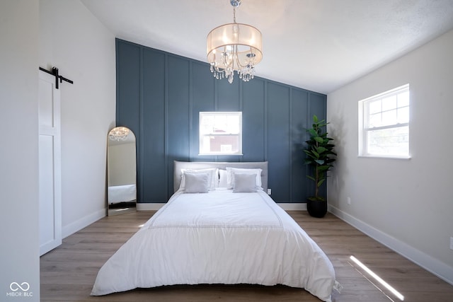 bedroom featuring a notable chandelier, a barn door, and light wood-type flooring