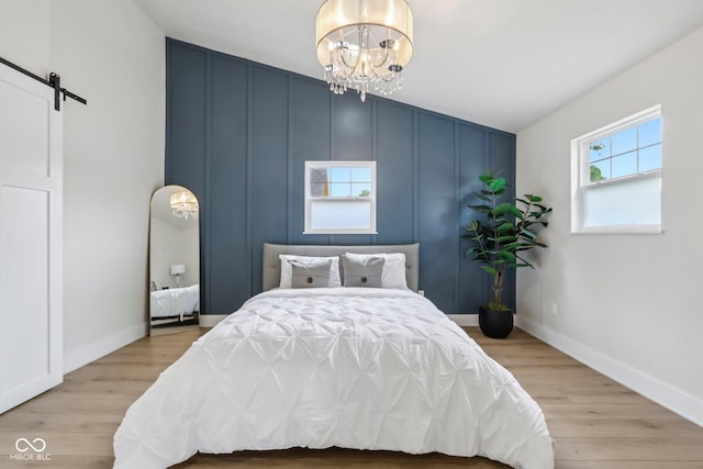 560 Jefferson Ave, Indianapolis, IN 46201 - bedroom with a chandelier, wood finished floors, a barn door, a decorative wall, and baseboards
