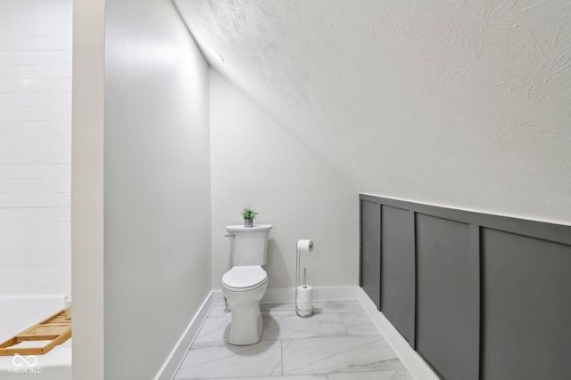 560 Jefferson Ave, Indianapolis, IN 46201 - bathroom featuring a textured ceiling, toilet, marble finish flooring, vaulted ceiling, and a bath