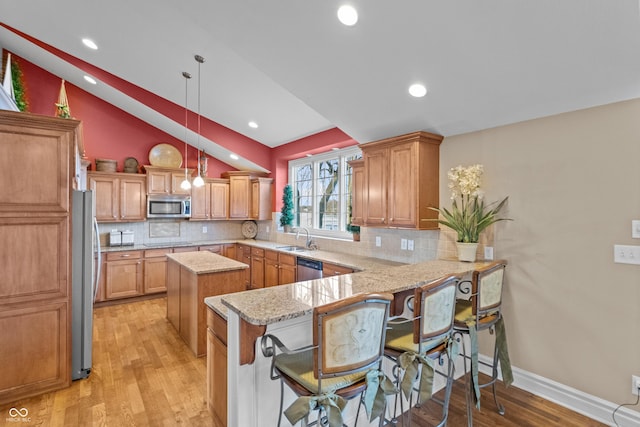 kitchen featuring sink, hanging light fixtures, stainless steel appliances, kitchen peninsula, and a breakfast bar area