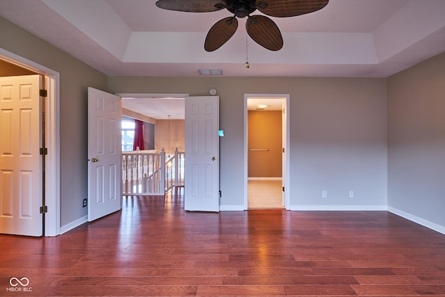 spare room with ceiling fan, a raised ceiling, and dark wood-type flooring