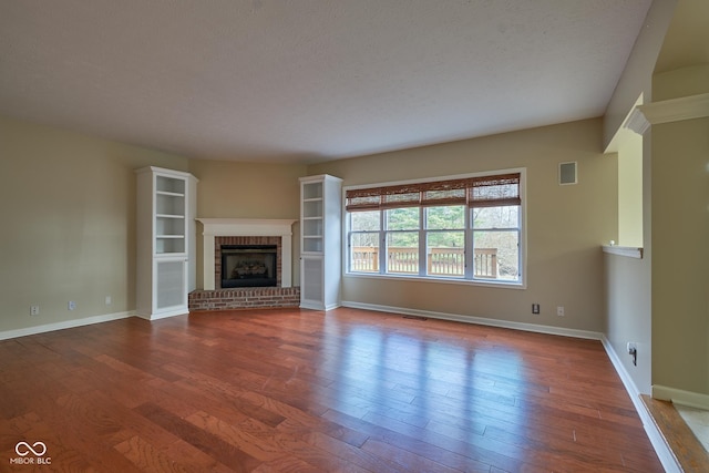 unfurnished living room featuring wood-type flooring, a textured ceiling, and a brick fireplace