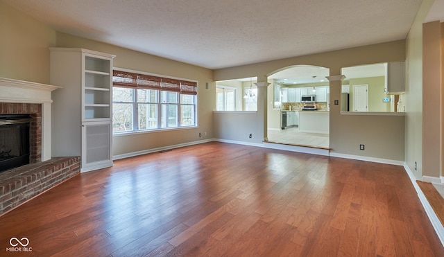 unfurnished living room featuring a textured ceiling, light hardwood / wood-style floors, a fireplace, and decorative columns