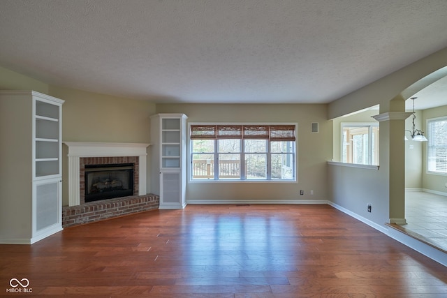 unfurnished living room featuring a textured ceiling, dark hardwood / wood-style floors, and a brick fireplace