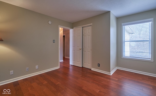 unfurnished bedroom featuring a textured ceiling, a closet, and dark wood-type flooring