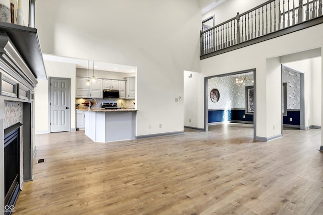 unfurnished living room featuring sink, a towering ceiling, a chandelier, and light wood-type flooring