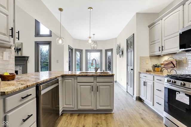 kitchen featuring light stone countertops, sink, tasteful backsplash, light hardwood / wood-style flooring, and appliances with stainless steel finishes