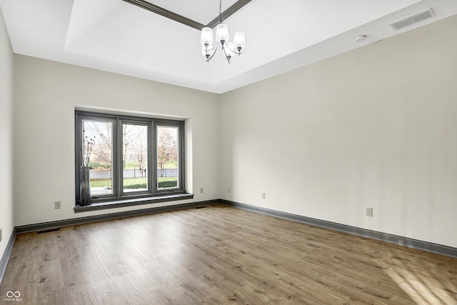 spare room featuring wood-type flooring, a tray ceiling, and a chandelier