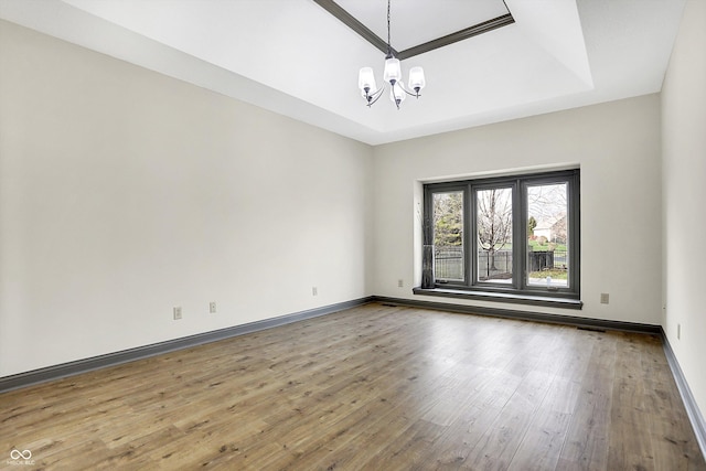 spare room with wood-type flooring, a tray ceiling, and an inviting chandelier