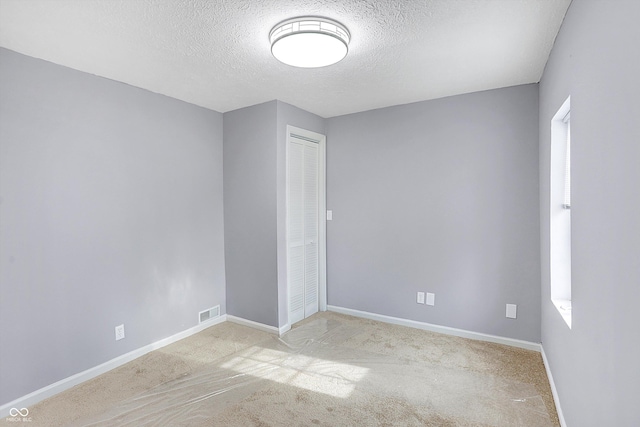 empty room with light colored carpet and a textured ceiling