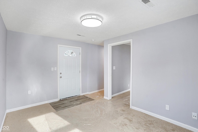 foyer entrance featuring light colored carpet and a textured ceiling