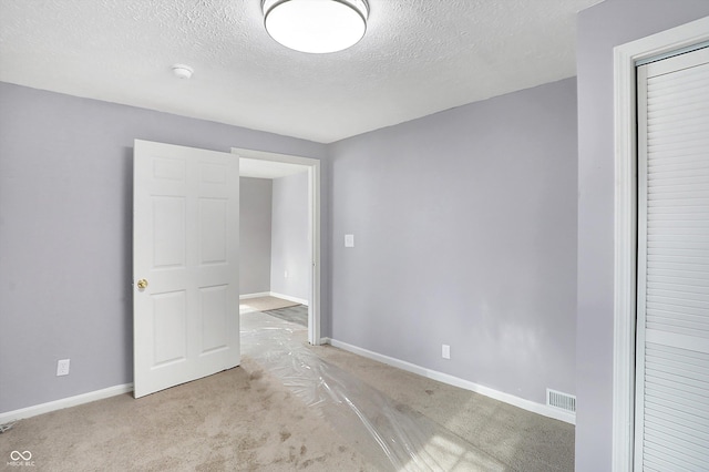 spare room featuring a textured ceiling and light colored carpet